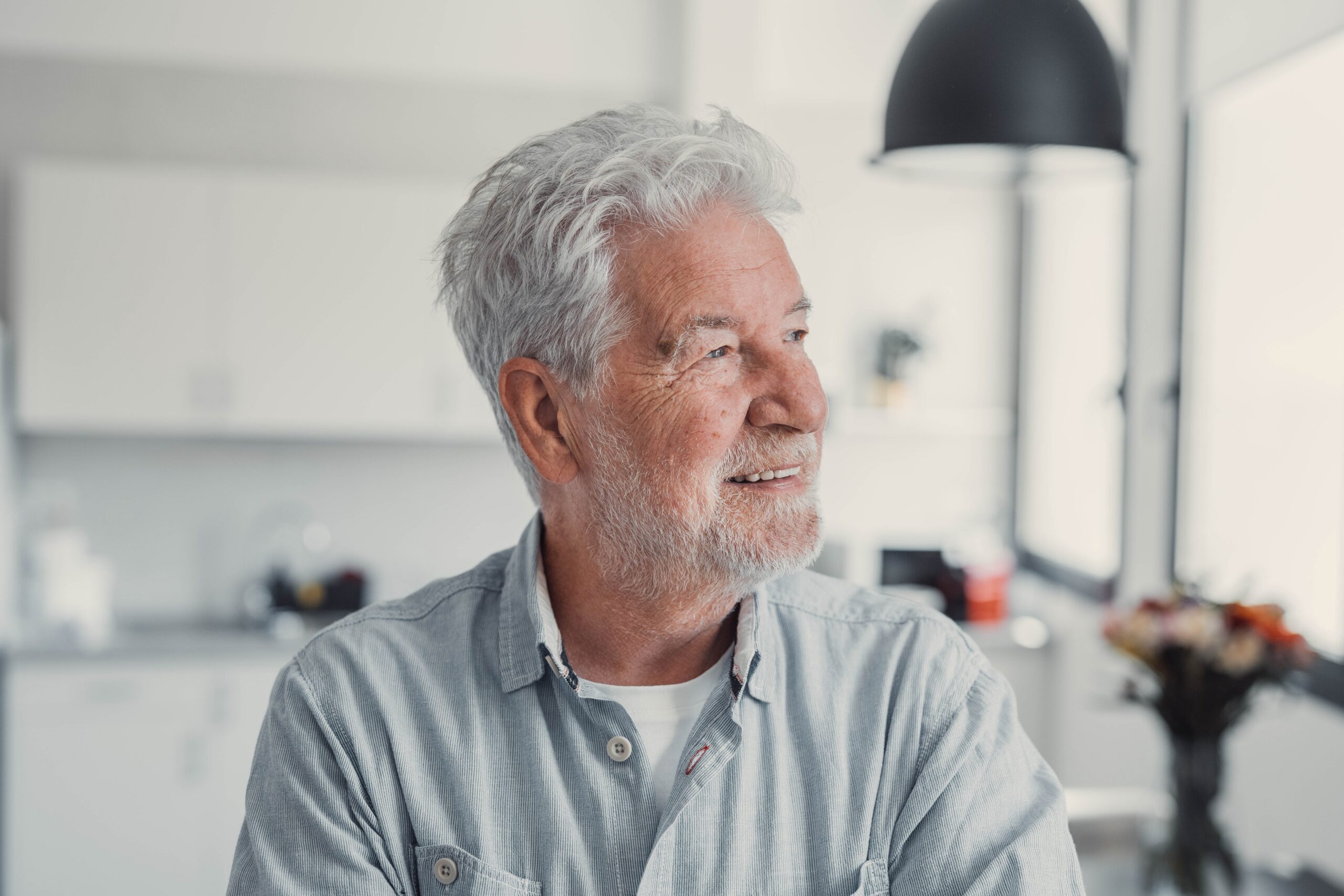 Elderly man stands by the window smiling while looking outside